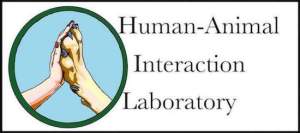 Human-Animal Interaction Laboratory logo (human hand and dog paw palm to palm in circle with blue background and green border